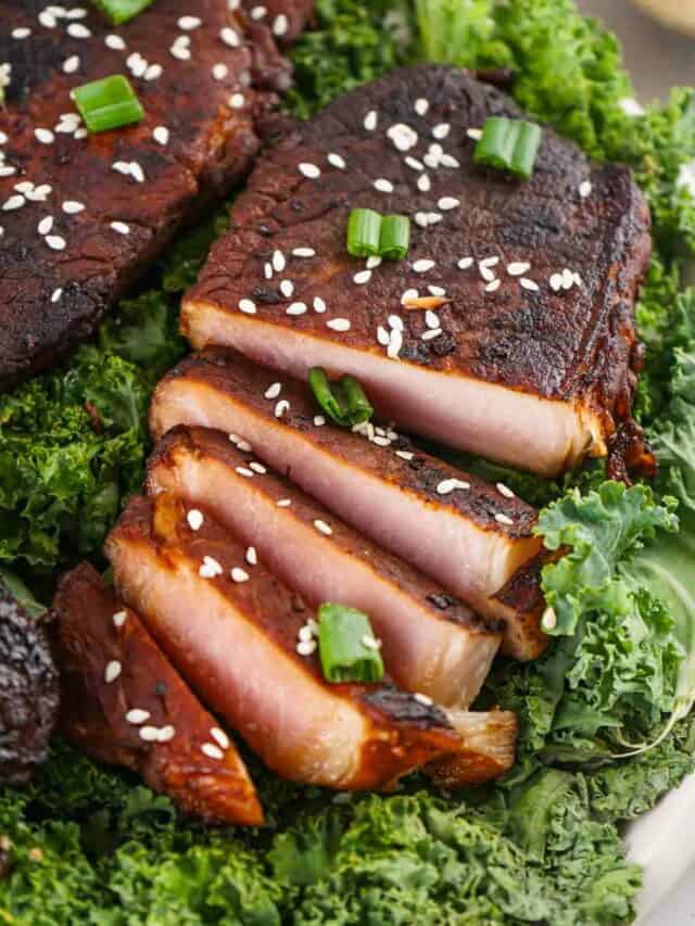 Sliced smoked pork belly with sesame seeds and green onions, served on a bed of kale.