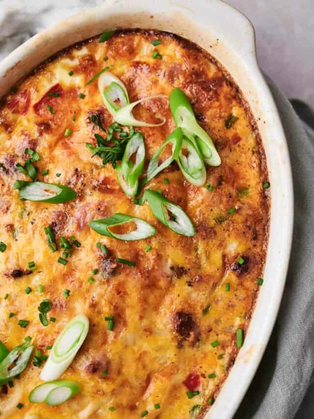 A baked casserole topped with melted cheese, green onions, and parsley in a white dish.