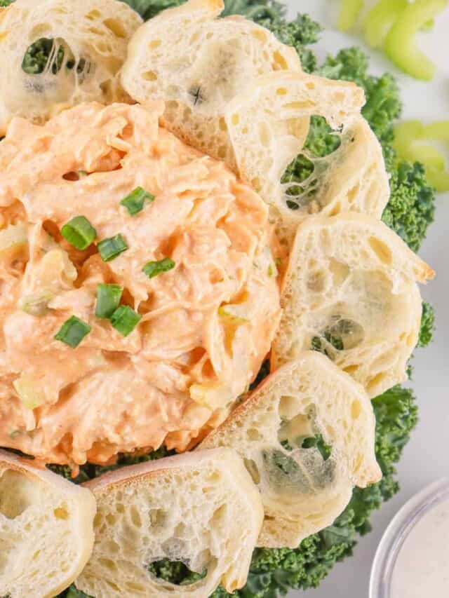 A bowl of carrot raisin salad served with slices of crusty bread and garnished with green onions, alongside broccoli florets.
