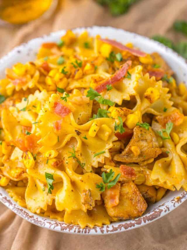 A bowl of bowtie pasta mixed with corn, diced chicken, herbs, and small pieces of bacon, garnished with chopped parsley.