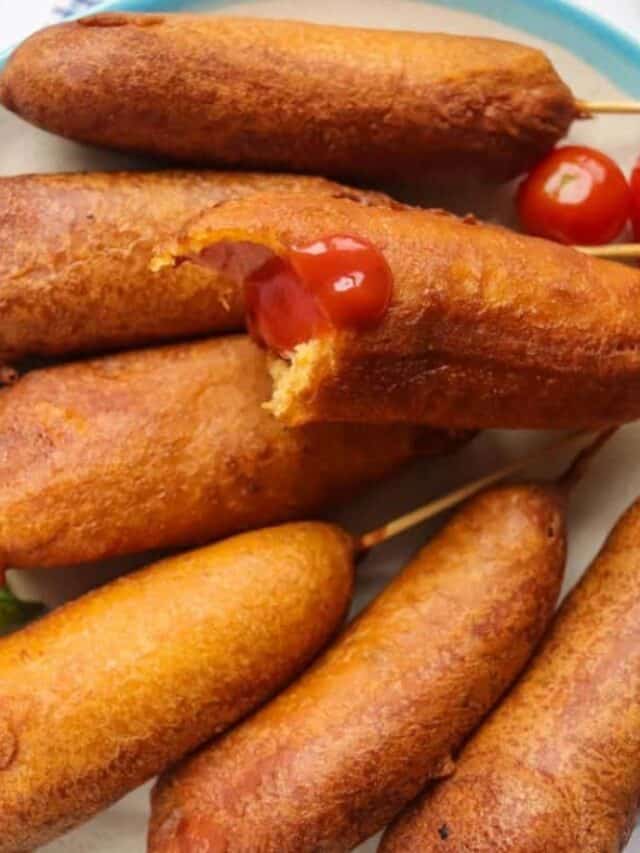 Corn dogs on sticks with one partially eaten, topped with ketchup.