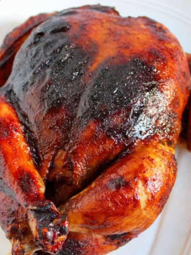 Close-up of a roasted chicken with a golden-brown, crispy skin displayed on a white plate.