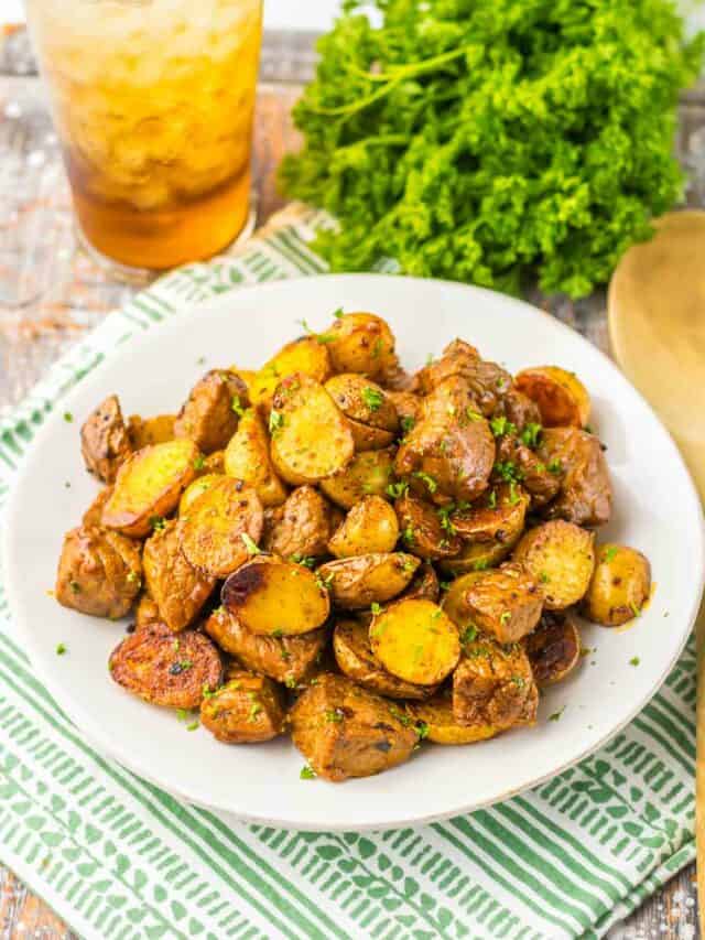 A plate of roasted potatoes garnished with parsley, served on a green and white striped napkin, with a glass of iced tea and fresh parsley in the background.