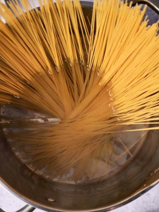 Uncooked spaghetti strands standing upright in a pot of boiling water.