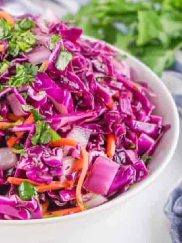 Colorful red cabbage salad with shredded carrots and herbs in a white bowl.
