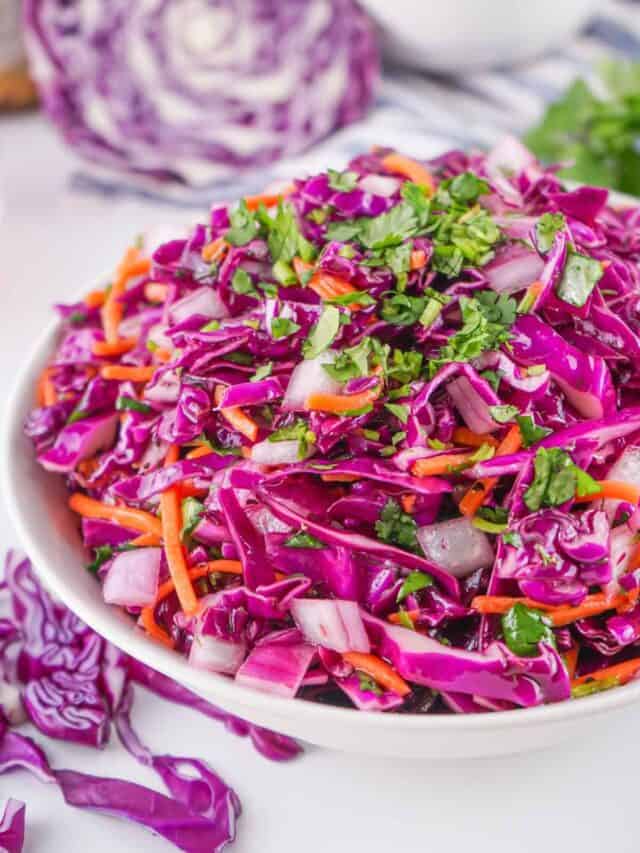 A bowl of fresh red cabbage coleslaw with shredded carrots and chopped herbs on a white and blue tablecloth.