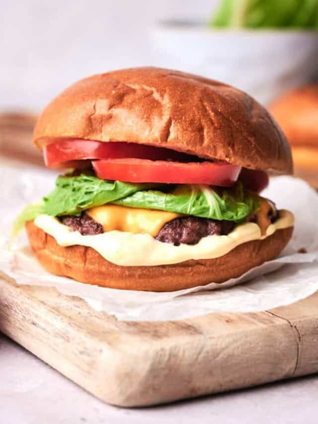 Smash burger on a board with a tomato on the side.