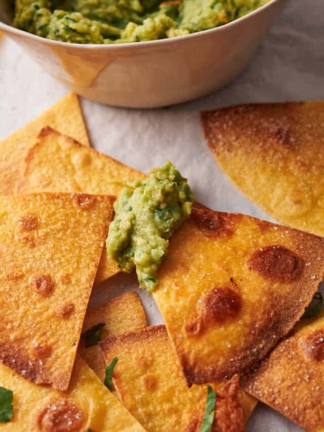 Tortilla chips with guacamole dip in a bowl. Some chips are topped with guacamole.