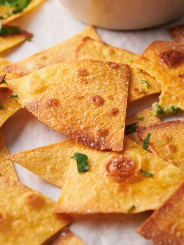 Close-up of golden-brown tortilla chips scattered on a surface, garnished with finely chopped herbs.