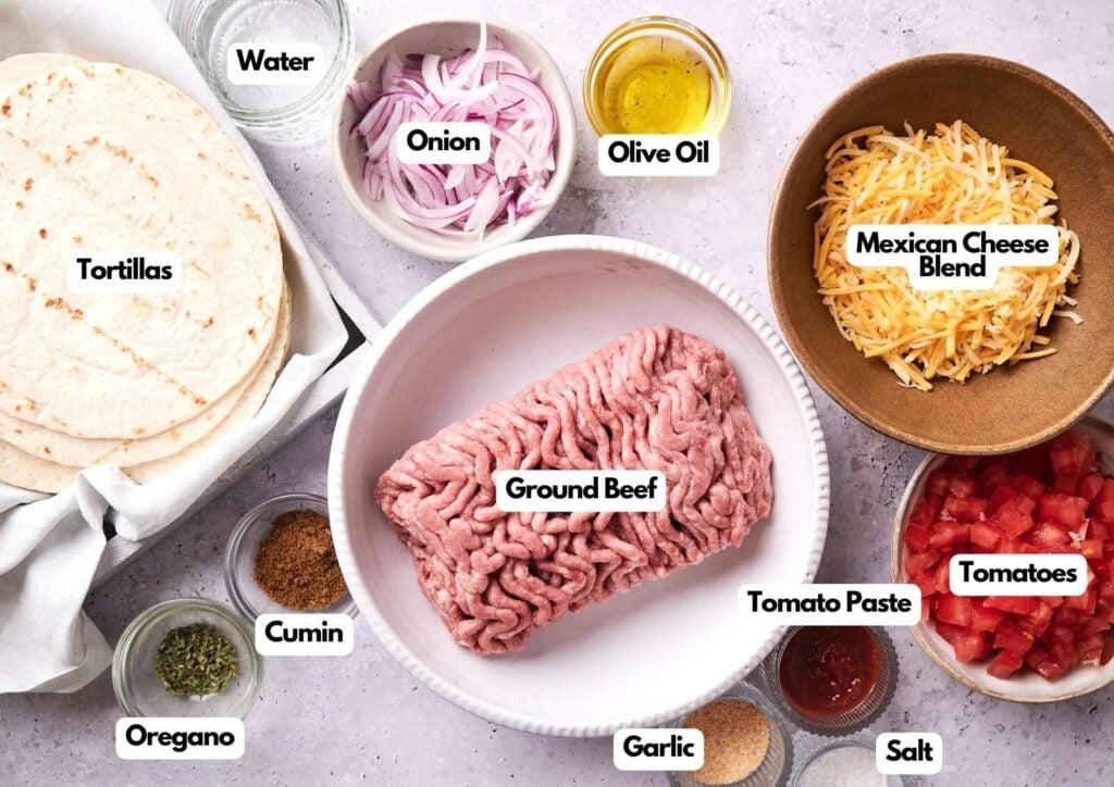 Ingredients for Beef Tacos are laid out, including tortillas, ground beef, onion, olive oil, Mexican cheese blend, tomatoes, tomato paste, cumin, oregano, garlic, salt, and water.