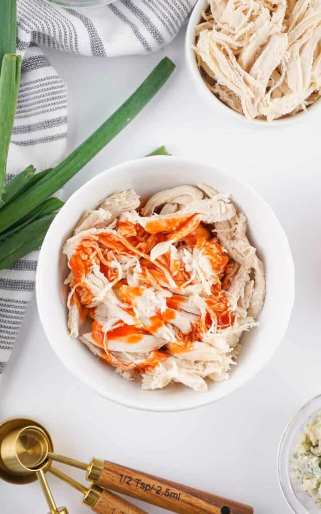Bowl of chicken topped with hot sauce on a kitchen counter.
