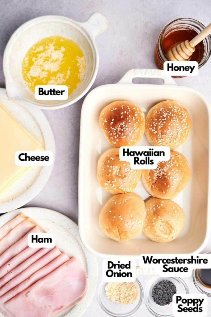 Ingredients for Ham and Cheese Sliders laid out, including butter, honey, cheese, Hawaiian rolls, ham, Worcestershire sauce, dried onion, and poppy seeds.