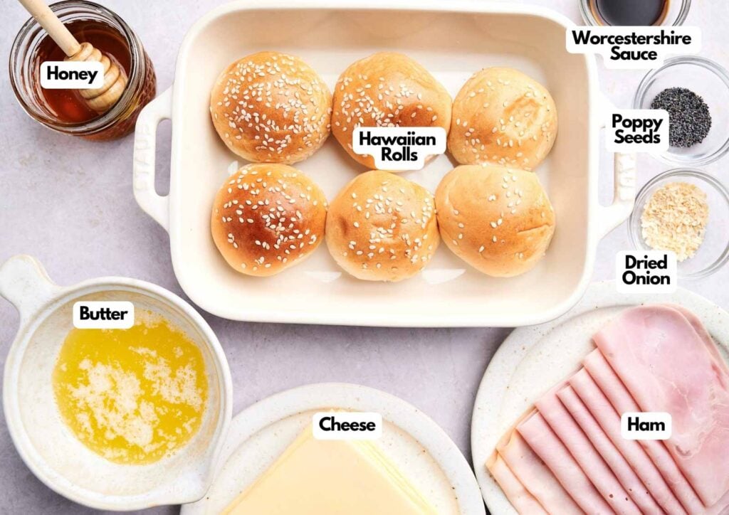 Top-down view of Ham and Cheese Sliders ingredients, including Hawaiian rolls, ham, cheese, butter, honey, Worcestershire sauce, poppy seeds, and dried onion.