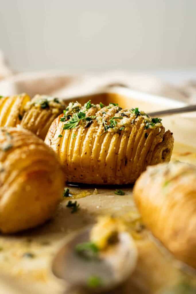 Close-up of Hasselback potatoes garnished with chopped parsley and grated parmesan cheese, with a spoon in the foreground.