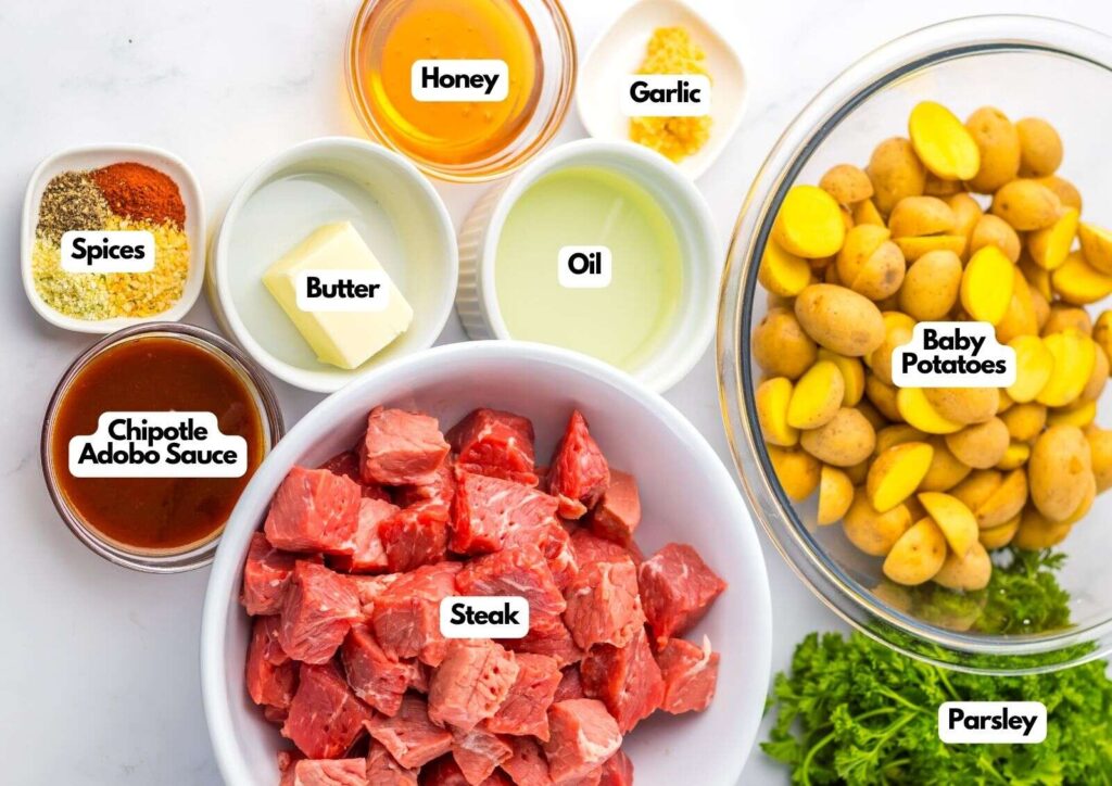 Labeled ingredients for Honey Chipotle Steak and Potatoes: steak cubes, baby potatoes, parsley, chipotle adobo sauce, spices, honey, butter, oil, and minced garlic in bowls.