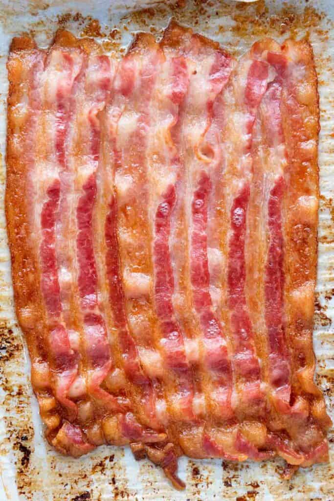 Several strips of cooked bacon on a tray of loaded tater tots.