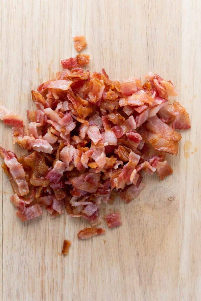 Chopped crispy bacon pieces on a wooden cutting board.