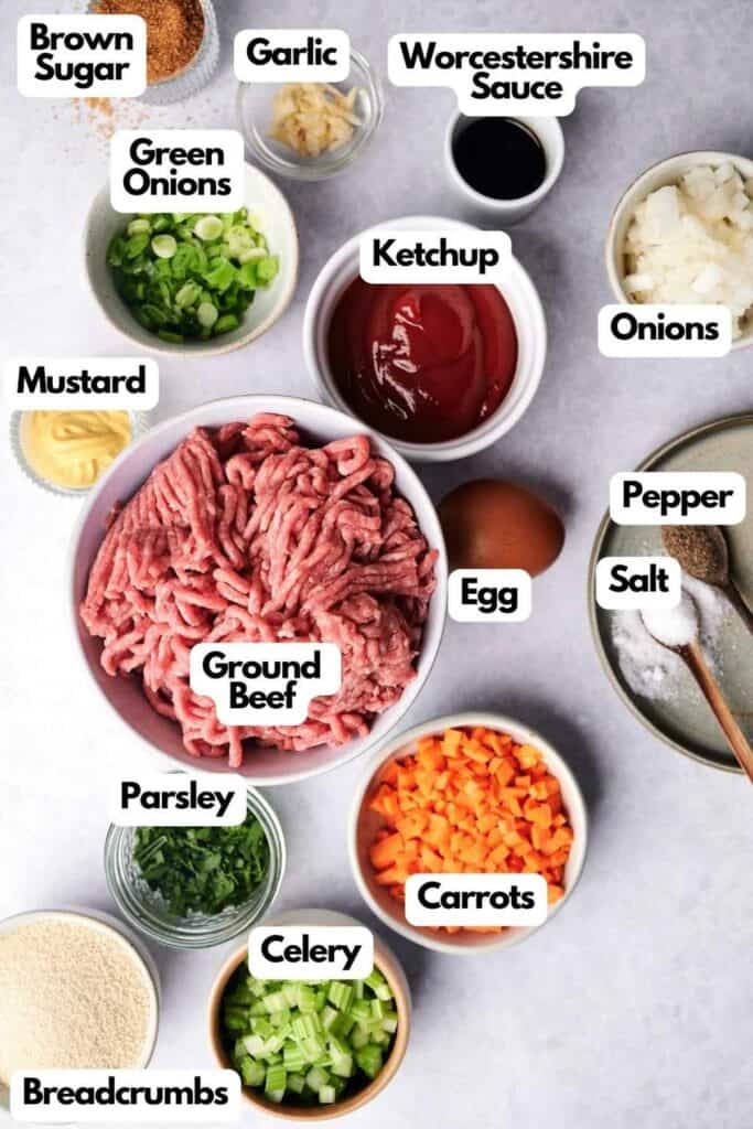 Top view of various labeled ingredients for meatloaf, including ground beef, egg, ketchup, Worcestershire sauce, garlic, onions, green onions, brown sugar, mustard, pepper, salt, carrots, celery, parsley, and breadcrumbs.