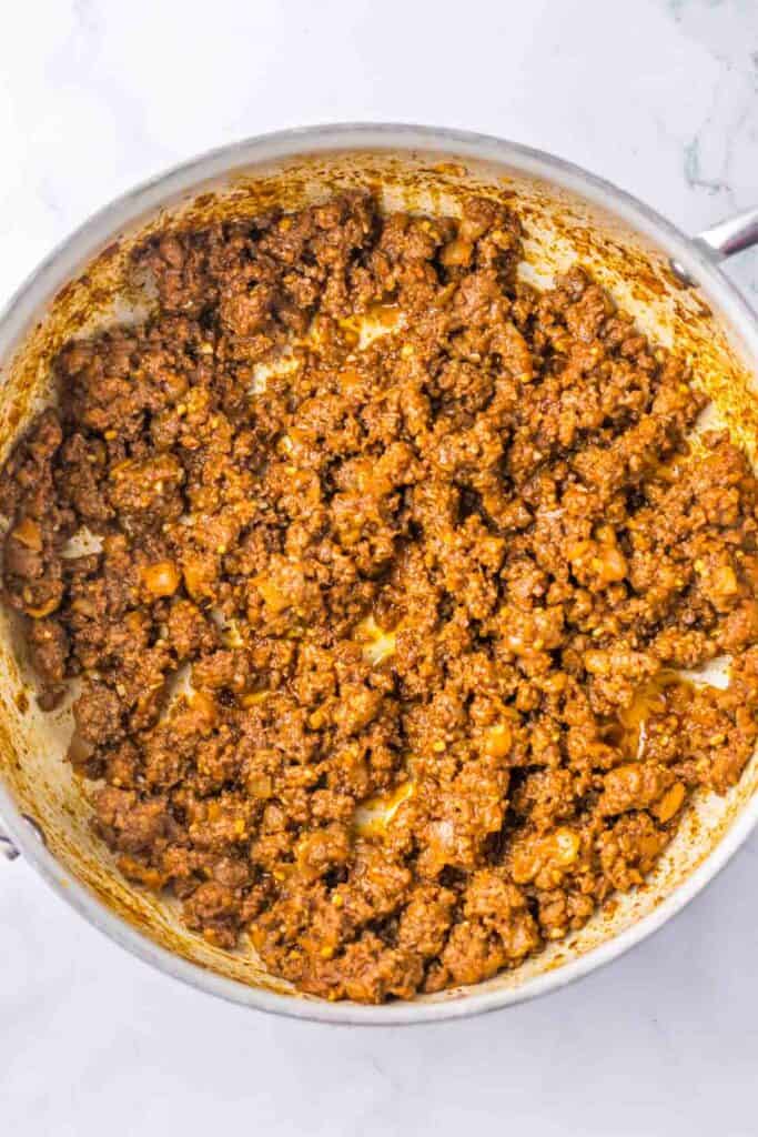 A pot filled with cooked ground meat seasoned with spices, perfect for making sloppy joe stuffed peppers, set on a white background.