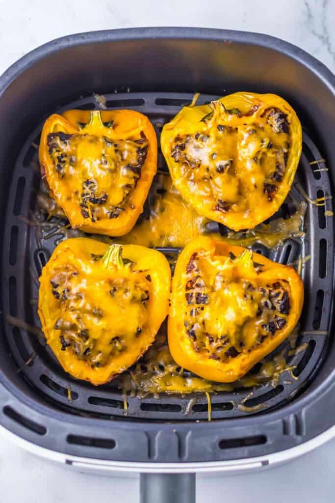 Four yellow bell peppers are transformed into sloppy joe stuffed peppers, brimming with a flavorful ground meat mixture and crowned with melted cheese, all perfectly cooked in an air fryer basket.