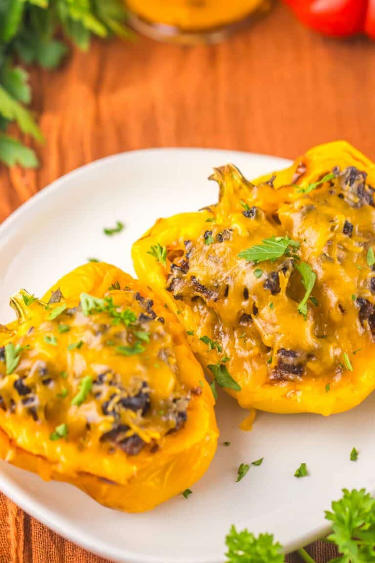 A white plate with two sloppy joe stuffed yellow bell peppers topped with melted cheese and garnished with fresh parsley.