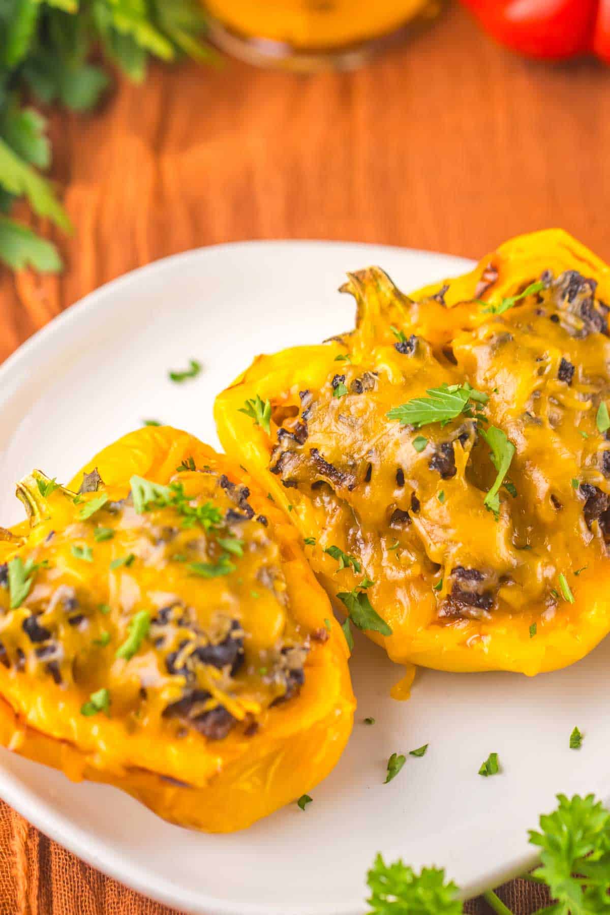 A white plate with two sloppy joe stuffed yellow bell peppers topped with melted cheese and garnished with fresh parsley.