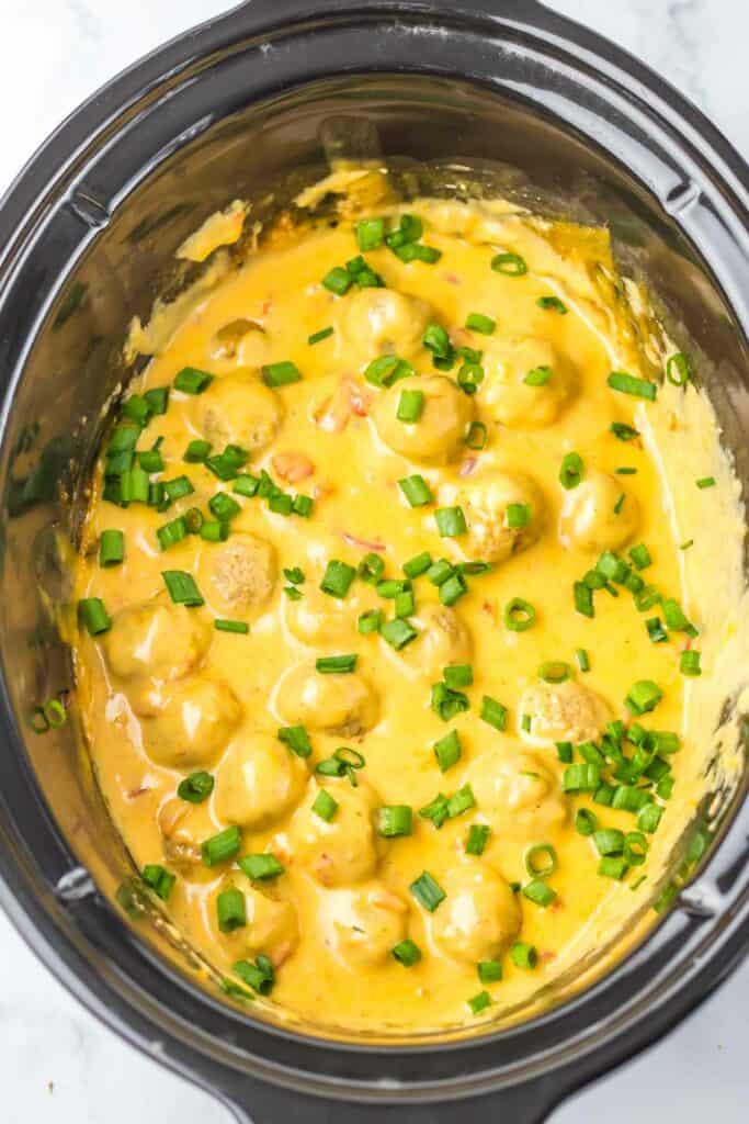 A slow cooker nacho meatballs, filled with creamy cheese sauce and topped with chopped green onions.