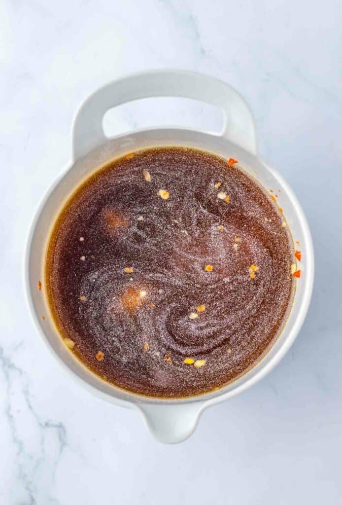 Top view of a white pot containing homemade sauce sprinkled with coarse sea salt, on a marble surface with slow cooker Salisbury steak meatballs.