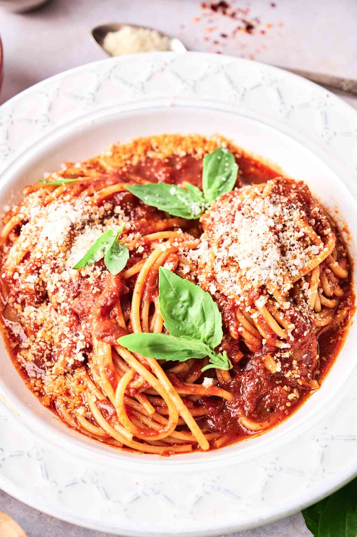 A plate of spaghetti with tomato sauce, basil leaves, and sprinkled parmesan cheese, served on a white plate.