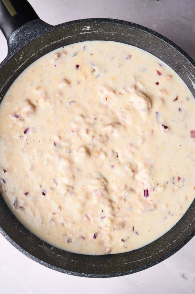 Creamy cheese sauce with bits of red onion in a black skillet.
