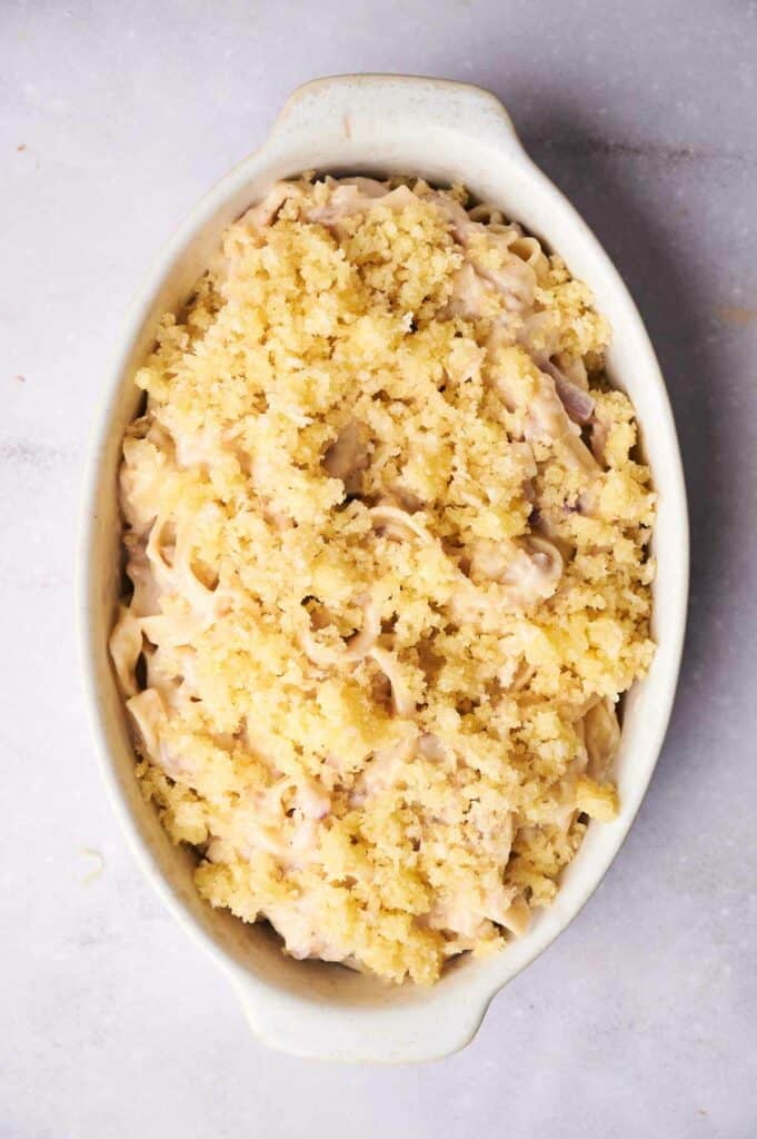 A creamy tuna noodle casserole topped with a golden breadcrumb crust, served in an oval, white baking dish.