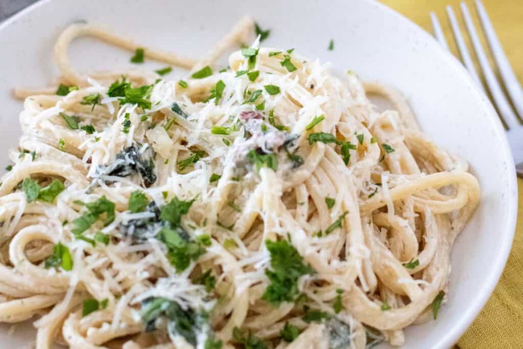 A plate of Creamy Tuscan Pasta garnished with chopped parsley and grated cheese sits on a table next to a fork.