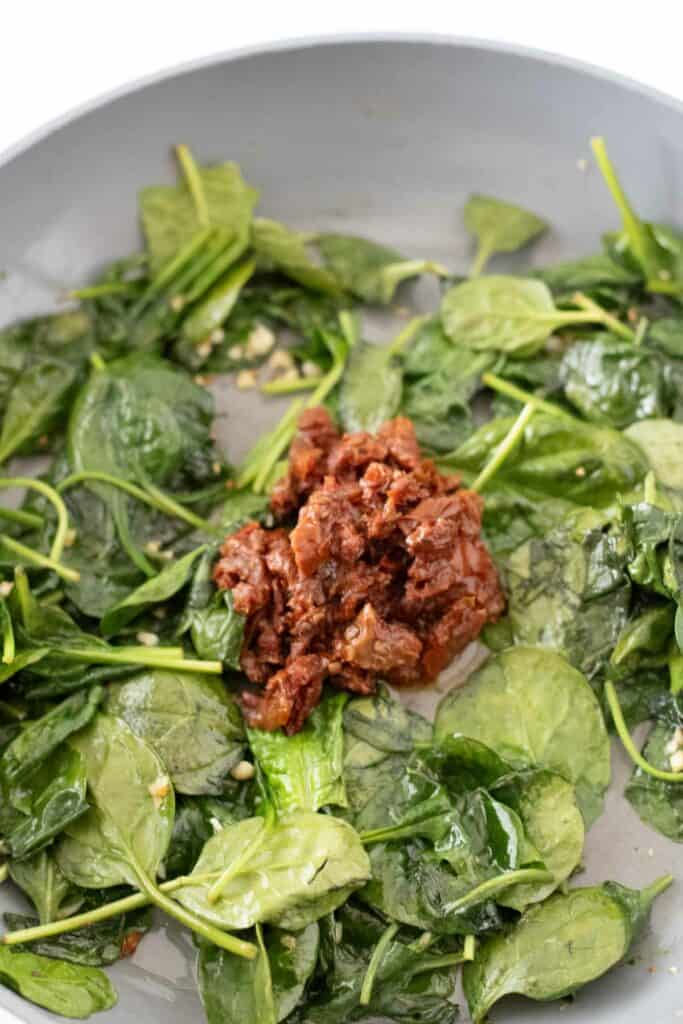 A pan with saut&eacute;ed spinach surrounding a mound of chopped sun-dried tomatoes at the center, evoking the vibrant flavors of Creamy Tuscan Pasta.
