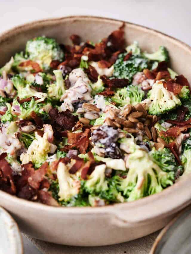 A bowl filled with a broccoli salad topped with chopped bacon, sunflower seeds, and a creamy dressing.