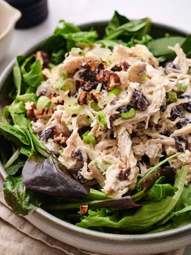 A bowl of chicken salad with chopped nuts, celery, and green onions served on a bed of mixed greens.
