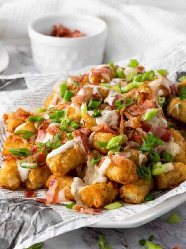 Loaded tater tots topped with melted cheese, bacon bits, and sliced green onions, served on a white plate with dipping sauce on the side.