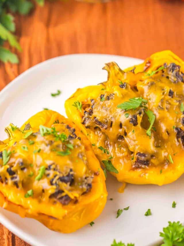 Two yellow bell peppers stuffed with a savory mixture, topped with melted cheese and garnished with herbs, served on a white plate.
