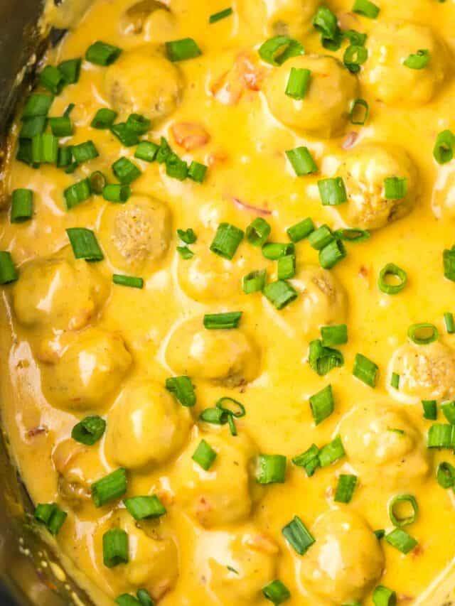 A dish of meatballs in yellow curry sauce, garnished with chopped green onions.