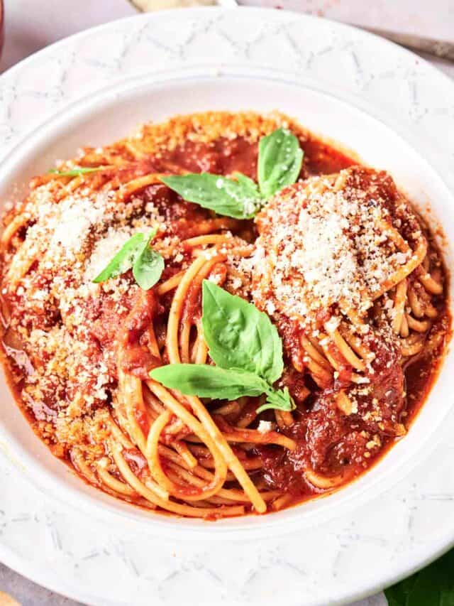 A plate of spaghetti topped with tomato sauce, grated cheese, and fresh basil leaves.