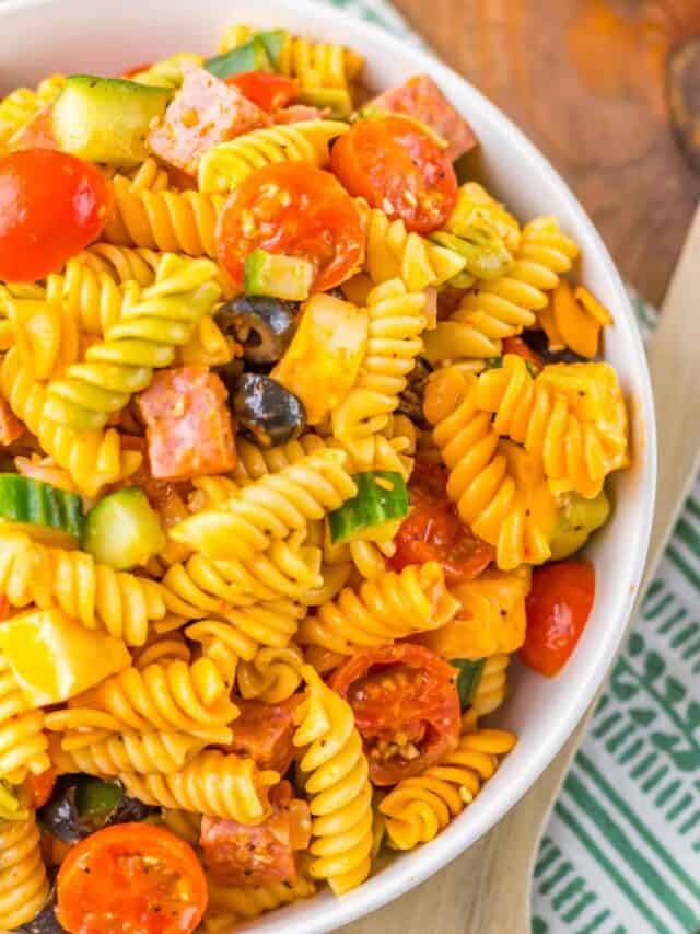 A bowl of rotini pasta salad with cherry tomatoes, olives, cucumbers, cheese cubes, and diced sausage.