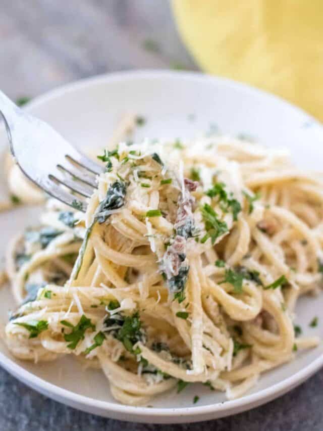 A plate of spaghetti pasta with creamy sauce, garnished with chopped parsley and grated cheese, being twirled on a fork.