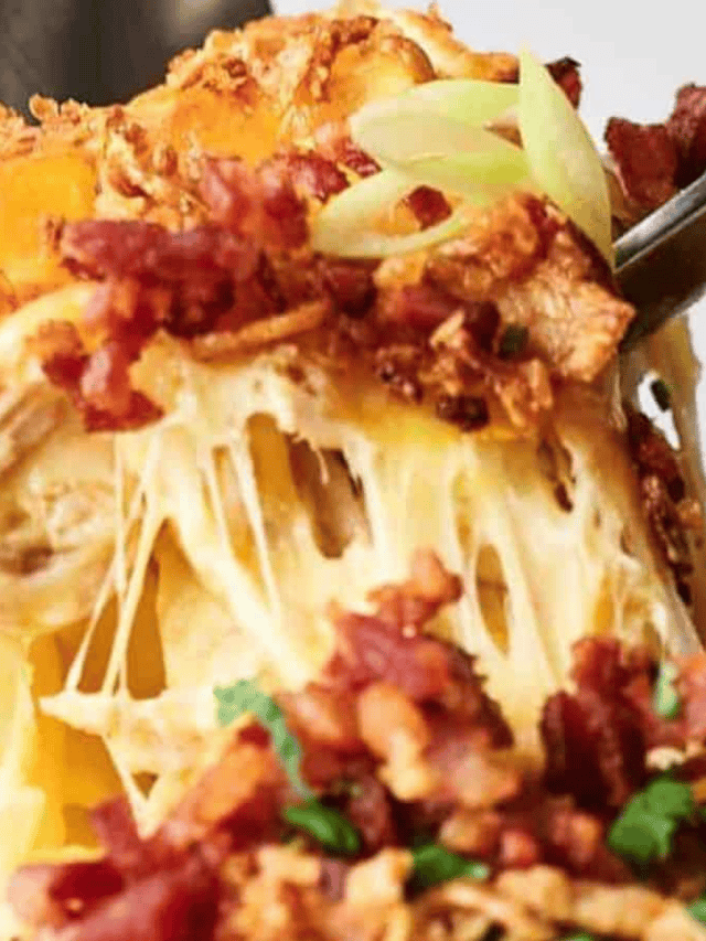 A close-up of a fork lifting a cheesy bite of baked potato topped with crispy bacon bits and chopped green onions.