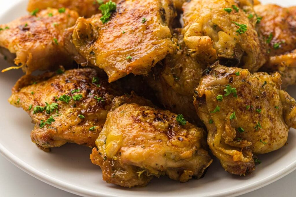 Plate of golden-brown air fryer chicken thighs garnished with chopped fresh parsley.