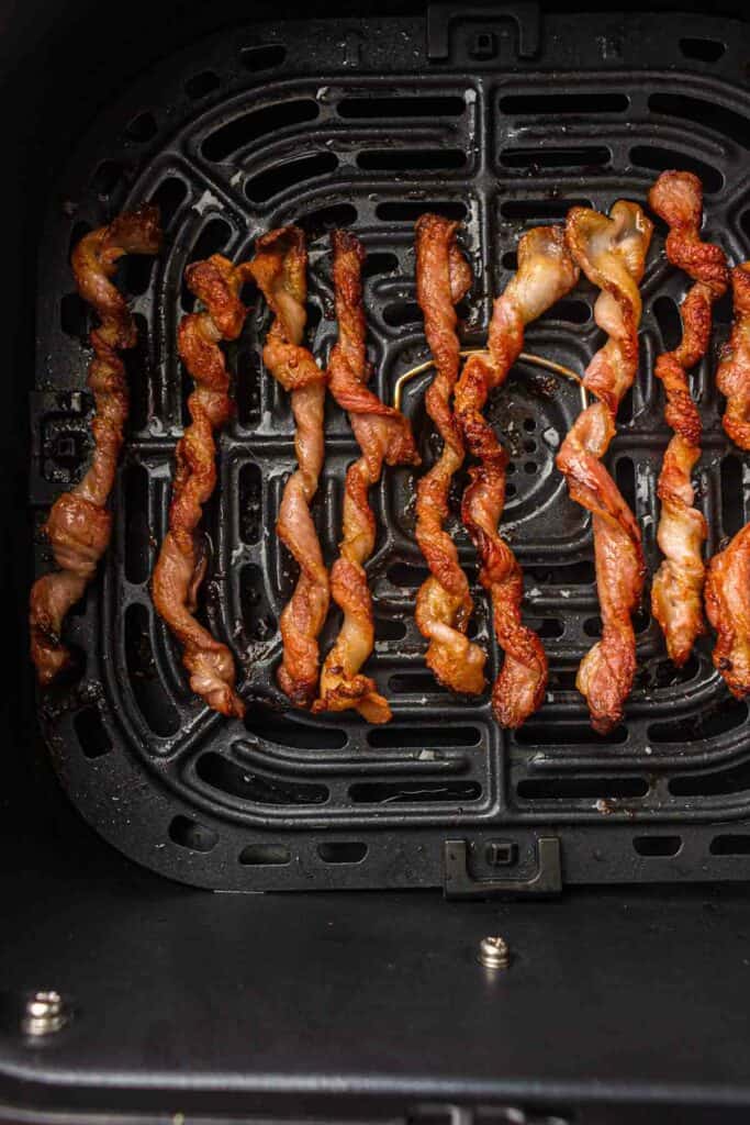 Strips of bacon twisted and cooked inside an air fryer basket.