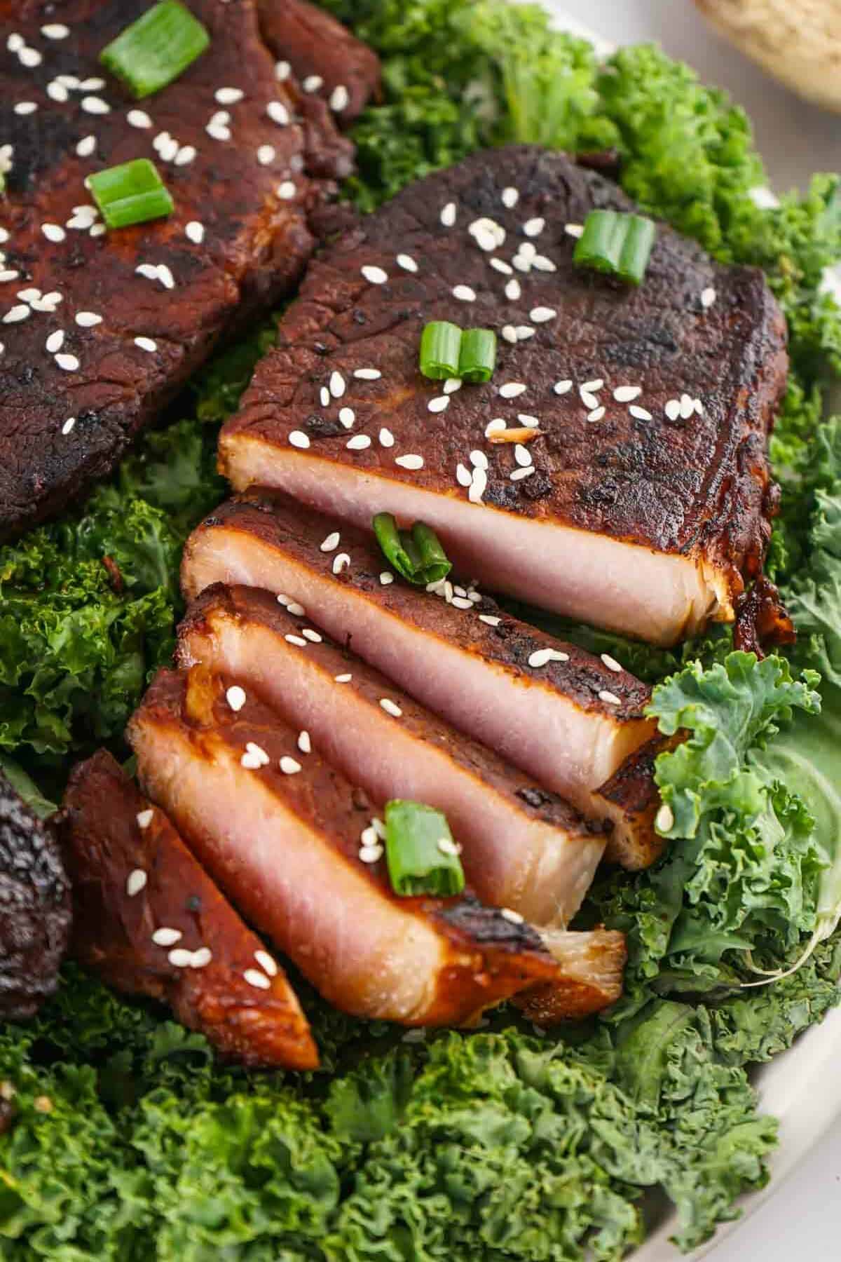Asian style pork chops garnished with sesame seeds and green onions, served on a bed of kale.