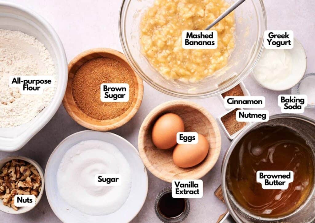Top-down view of labeled banana bread ingredients in bowls and jars, including flour, mashed bananas, sugar, brown sugar, eggs, nuts, vanilla extract, yogurt, spices, baking soda&mdash;and a splash of Patriotic Gumdrops for a festive twist.