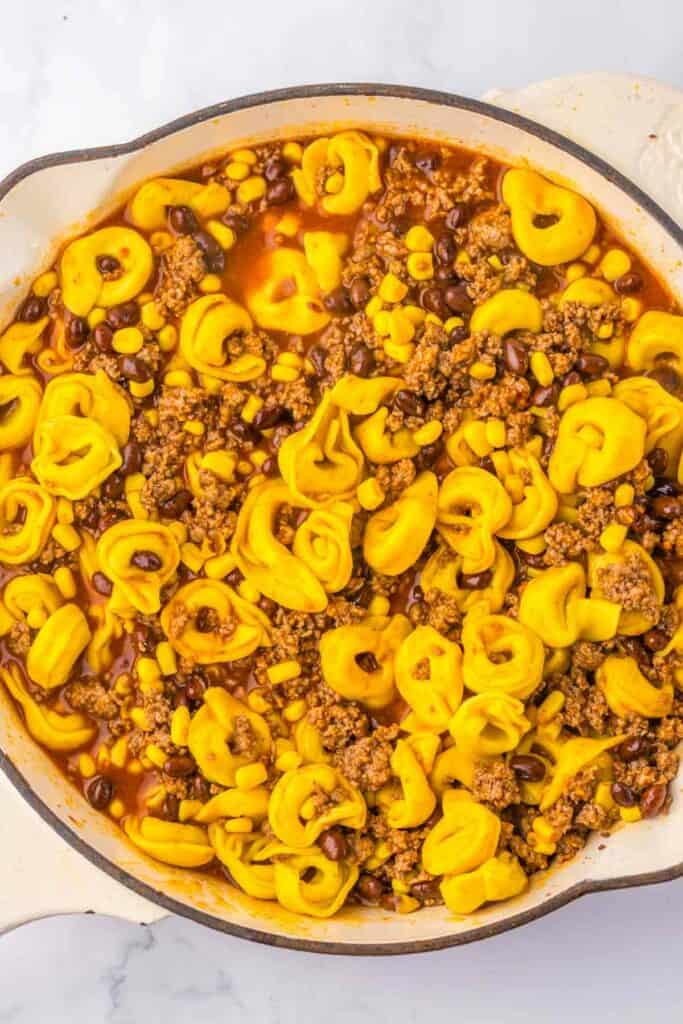 A skillet containing Beef Enchilada Tortellini, with ground meat, corn, and black beans in a tomato-based sauce.
