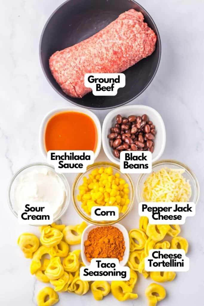 Ingredients laid out on a white background include ground beef, enchilada sauce, black beans, sour cream, corn, pepper jack cheese, taco seasoning, and cheese tortellini for a delicious Beef Enchilada Tortellini dish.