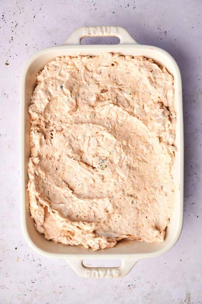 A rectangular dish filled with a creamy, buffalo mixture. The dish has handles on both ends and is placed on a light-colored surface.