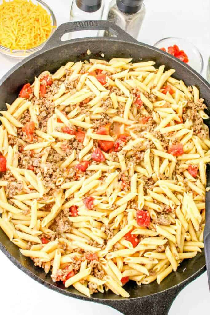 A skillet filled with cooked pasta, ground meat, and diced tomatoes, creating a delicious cheeseburger pasta delight.